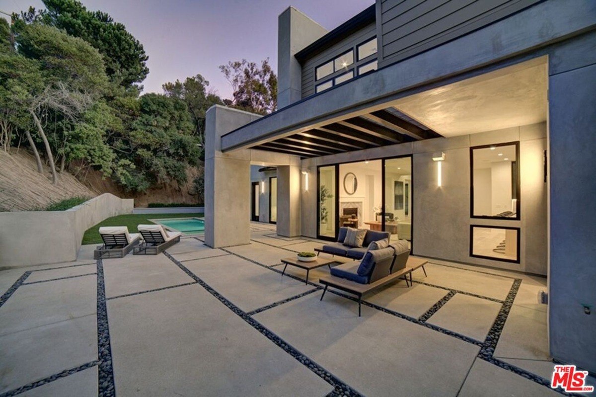 Open patio area with contemporary outdoor furniture overlooks the poolside, framed by concrete walls and lush greenery.