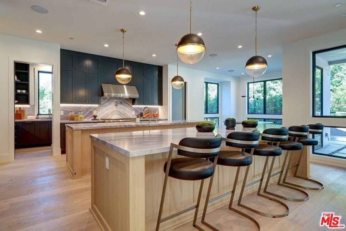 Modern kitchen layout features a large center island, stylish pendant lighting, and sleek black cabinets complemented by natural light from expansive windows.