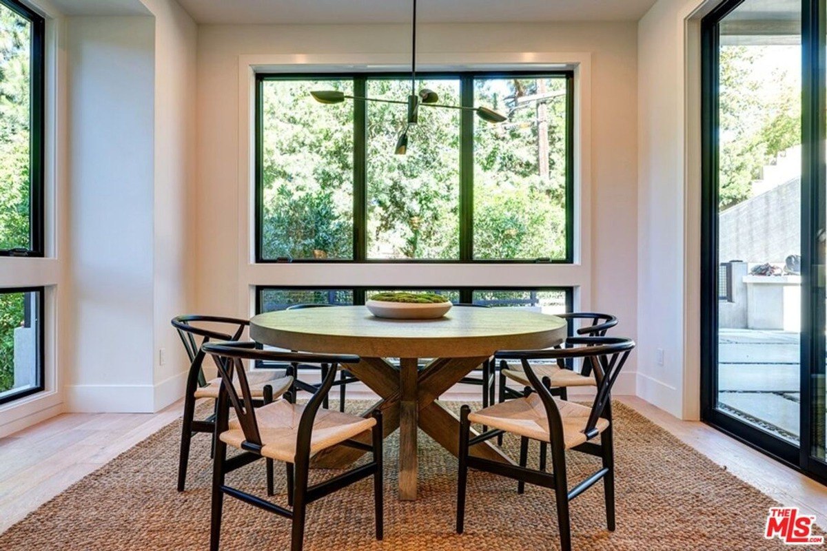 Bright breakfast nook includes a round wooden table, contemporary chairs, and floor-to-ceiling windows for an outdoor view.