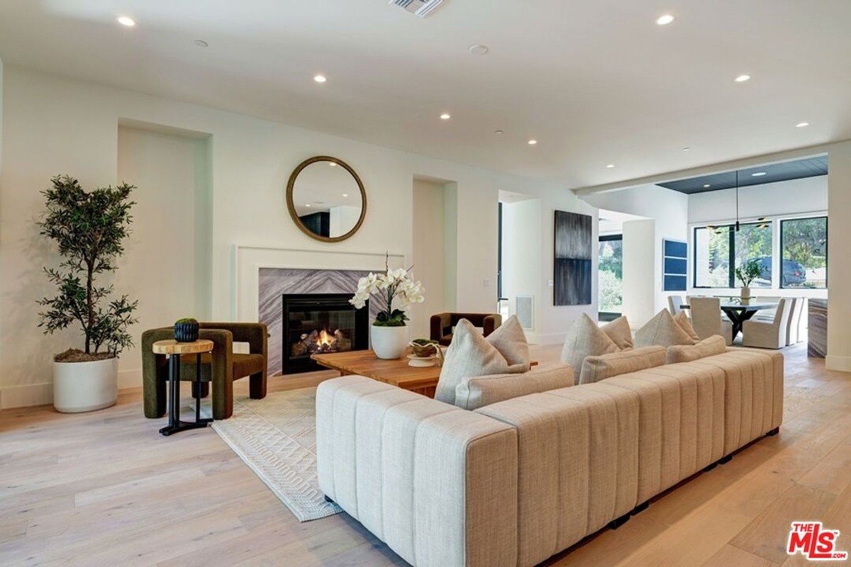 Open-concept living room showcases a cozy sectional, a central fireplace, and decorative accents like a wall mirror and lush indoor plant.