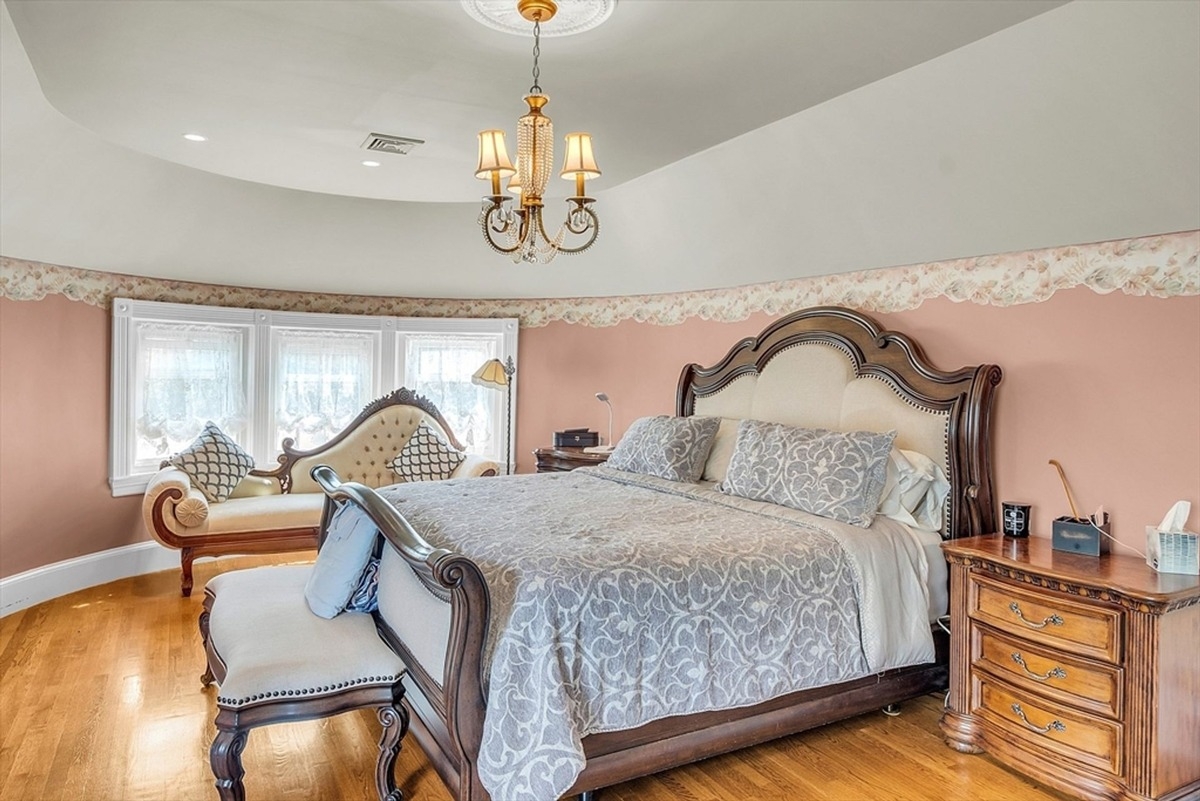 Primary bedroom highlights a wooden bed frame, chaise lounge, and soft pink walls.