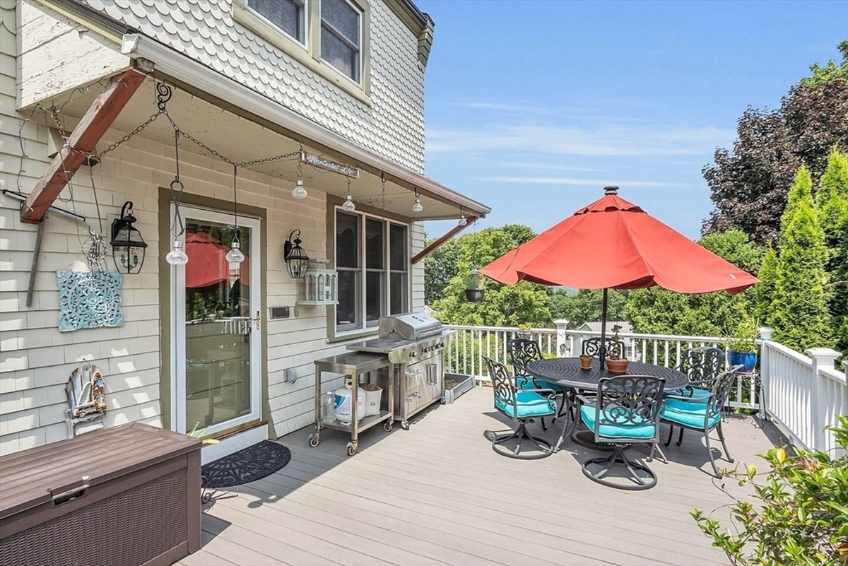 Outdoor patio features a red umbrella over a wrought iron dining set with a grill and hanging lanterns.