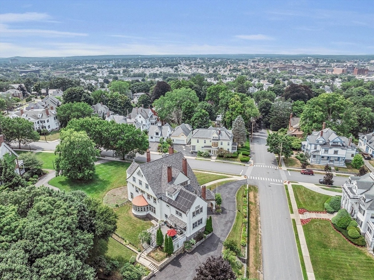 Aerial view highlights the house, surrounding neighborhood, and spacious green lawns.