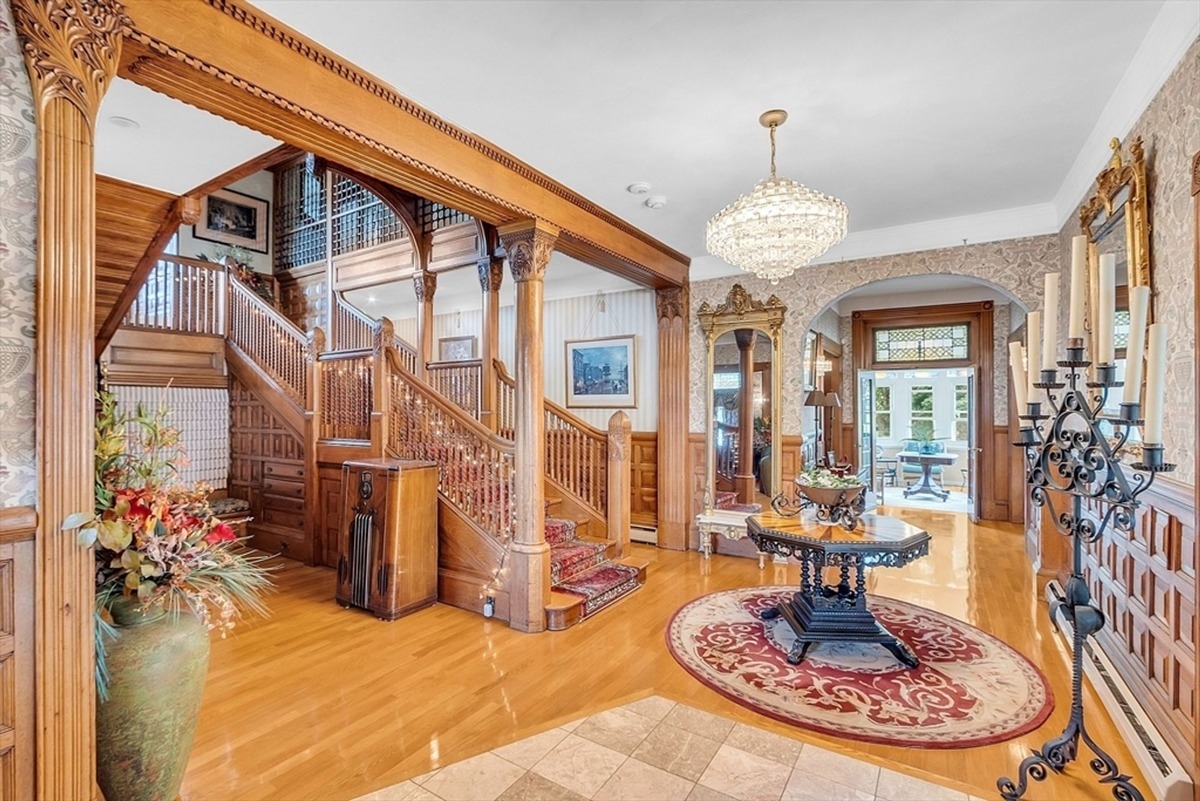 Grand staircase and foyer adorned with intricate woodwork and a chandelier.