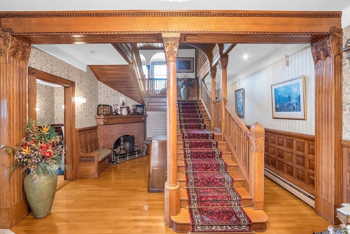 Red carpet staircase framed by decorative wooden columns and an ornate fireplace.