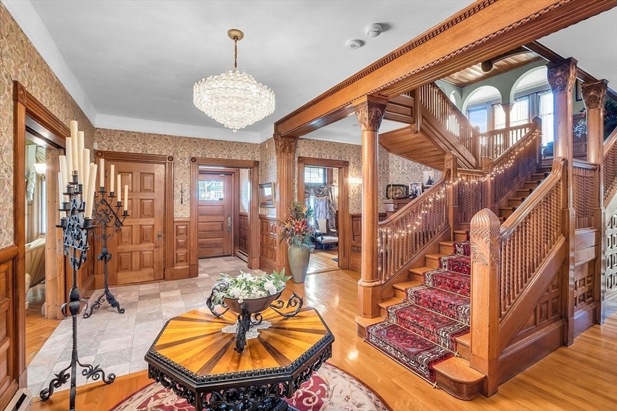 Spacious foyer with wooden details, a large chandelier, and access to multiple rooms.