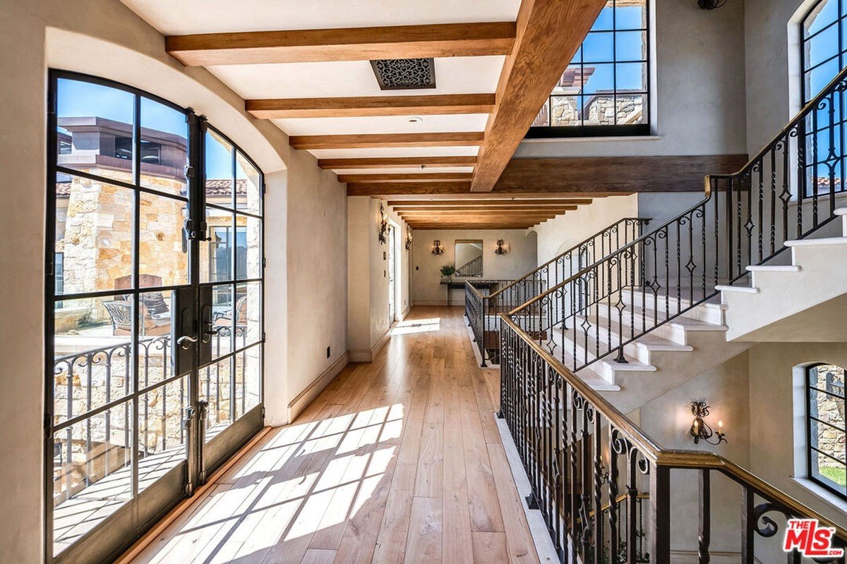 Hallway with iron-framed windows, wood beam ceilings, and natural light flooding in.