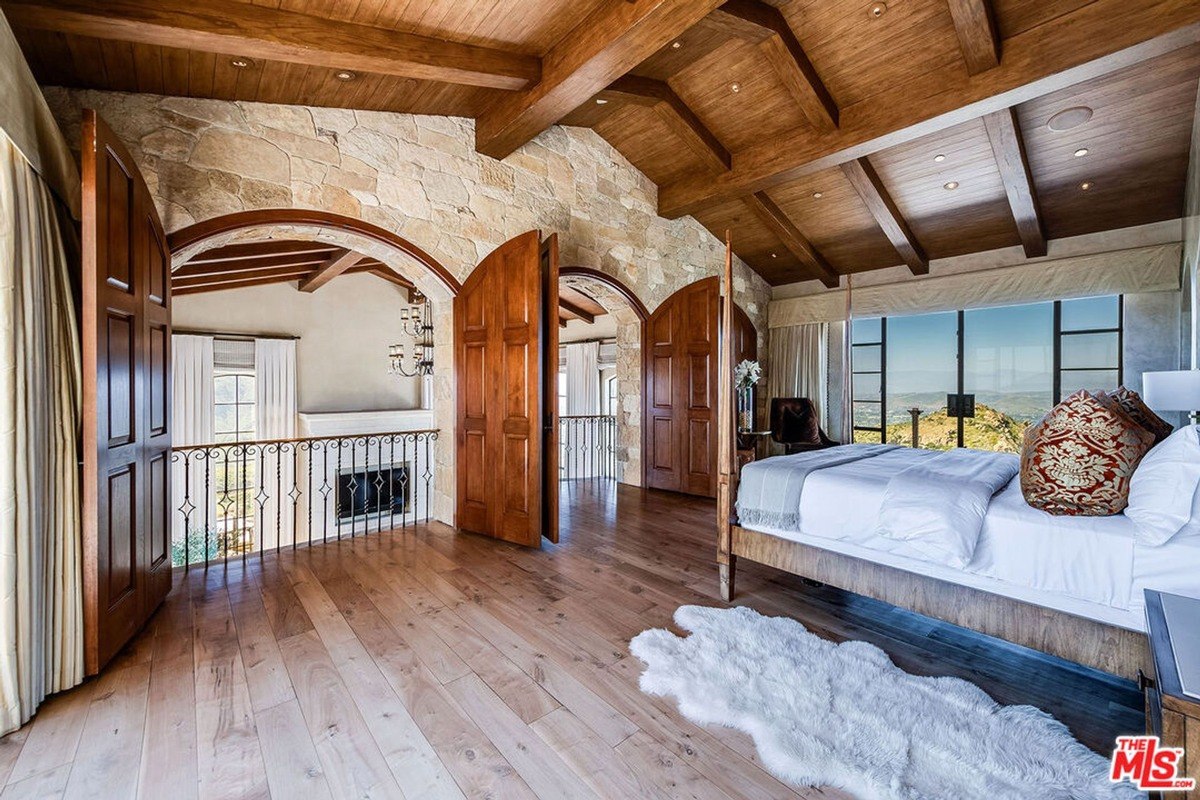 Bedroom suite featuring vaulted wood ceilings, stone accents, and an arched balcony opening.