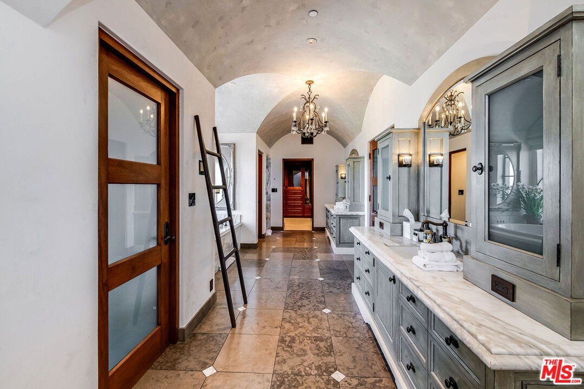 Luxurious bathroom with dual vanities, marble counters, and a vaulted ceiling with elegant lighting.