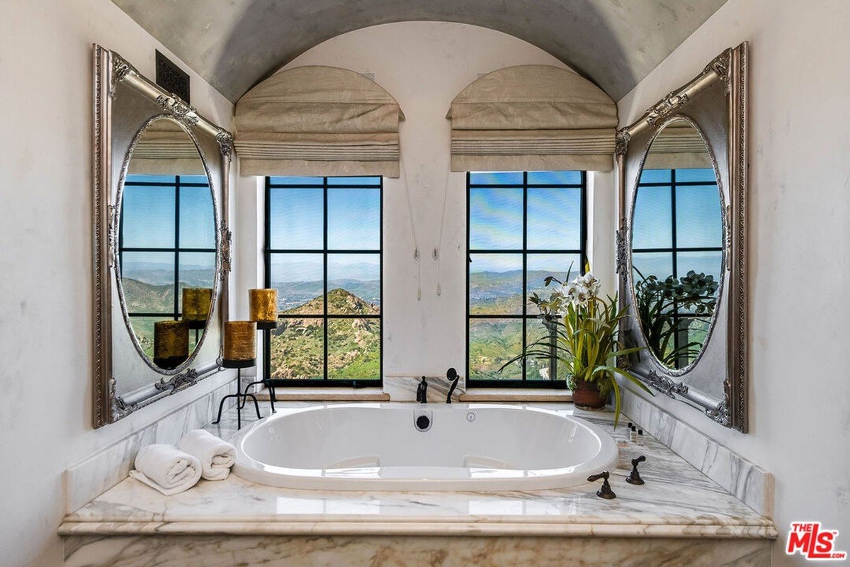 Elegant bathroom with marble finishes and a soaking tub framed by large windows offering panoramic mountain views.