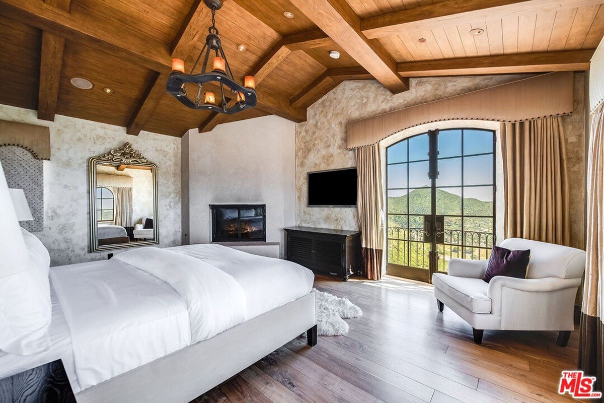 Spacious bedroom featuring vaulted wood-beamed ceilings, a fireplace, and glass doors leading to a balcony with scenic views.