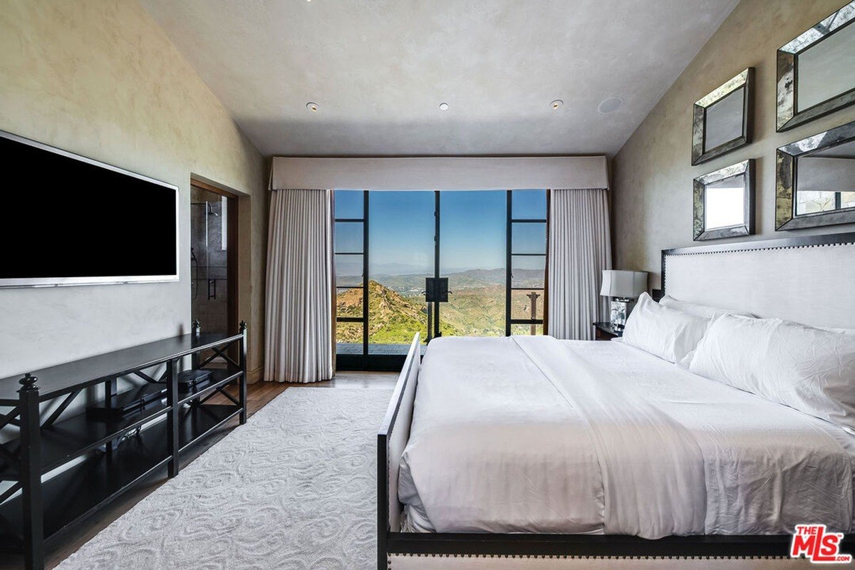 Modern bedroom designed with neutral tones, large windows, and unobstructed views of the surrounding hills.