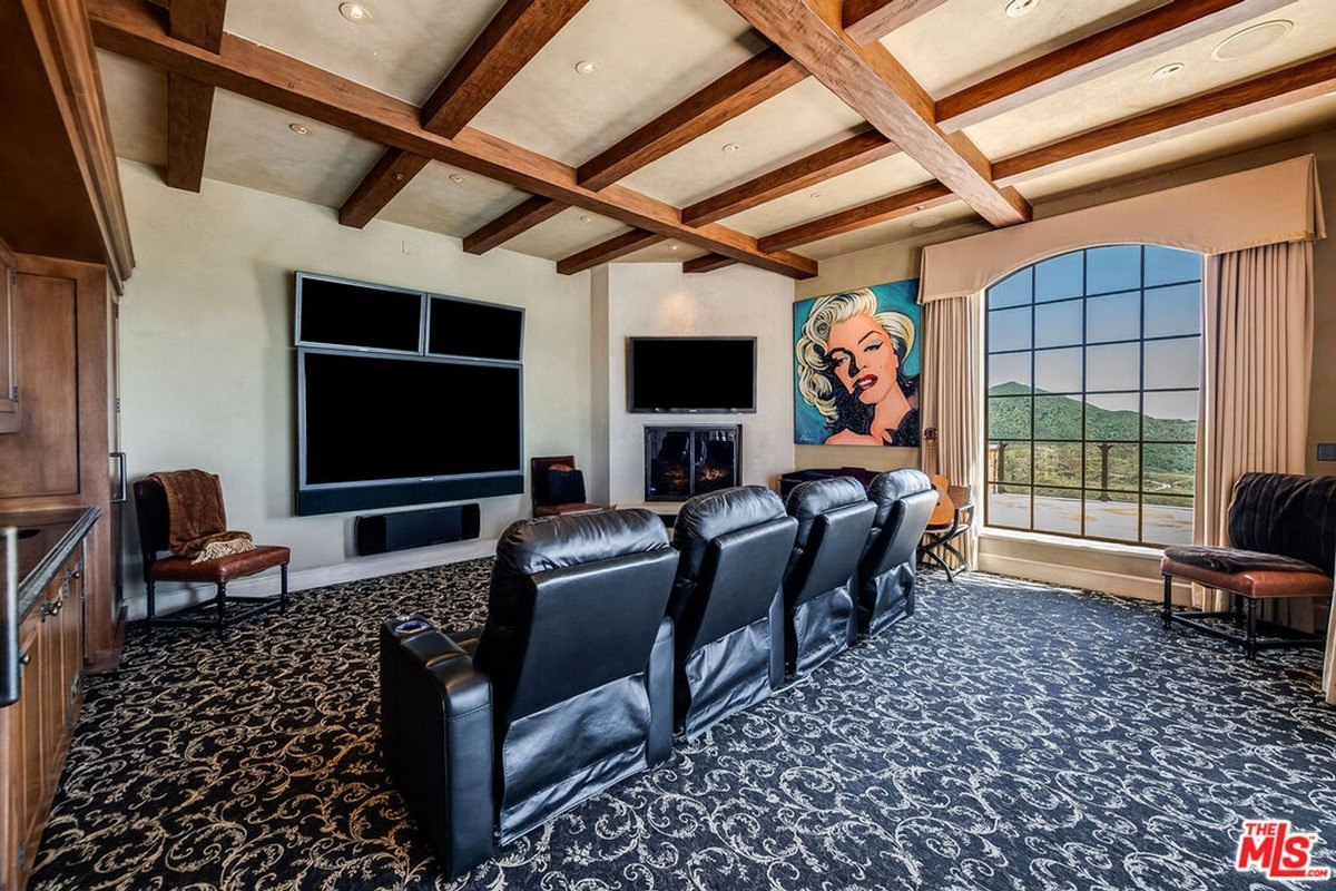 Cozy home theater with plush recliners, large entertainment screens, and exposed wooden beams.