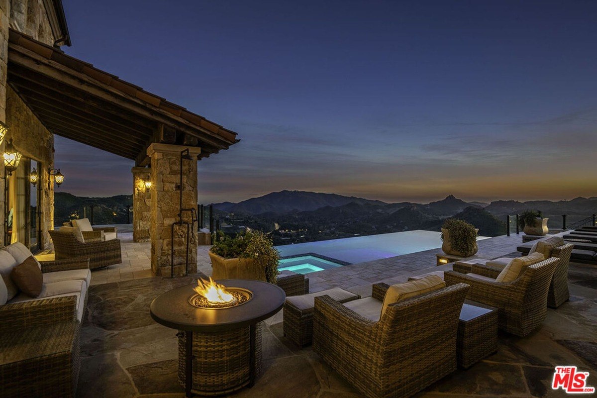 Infinity pool terrace with a fire pit, comfortable seating, and a backdrop of rolling hills and twilight skies.