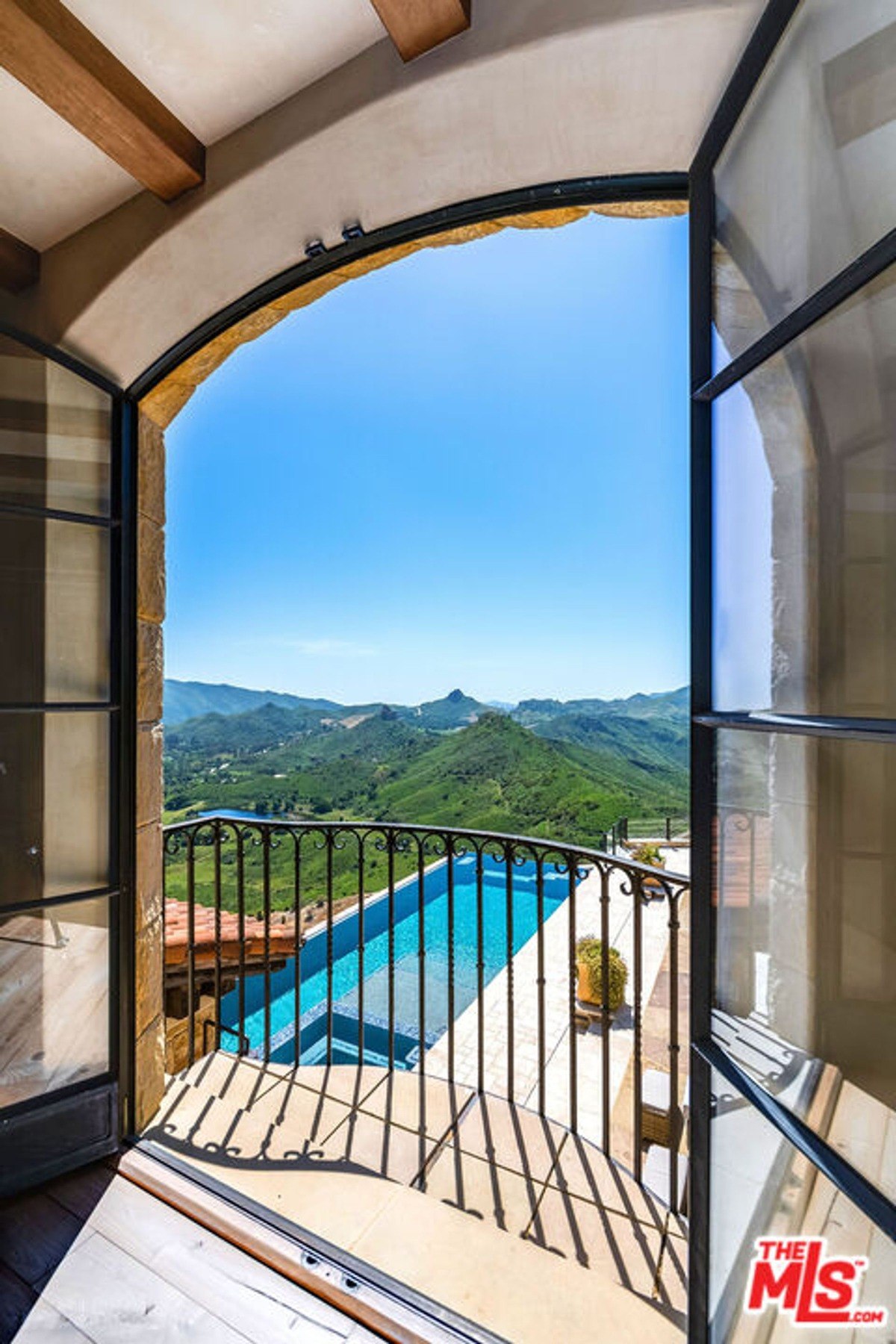 Arched doorway opens to a balcony overlooking a pool and mountain views.