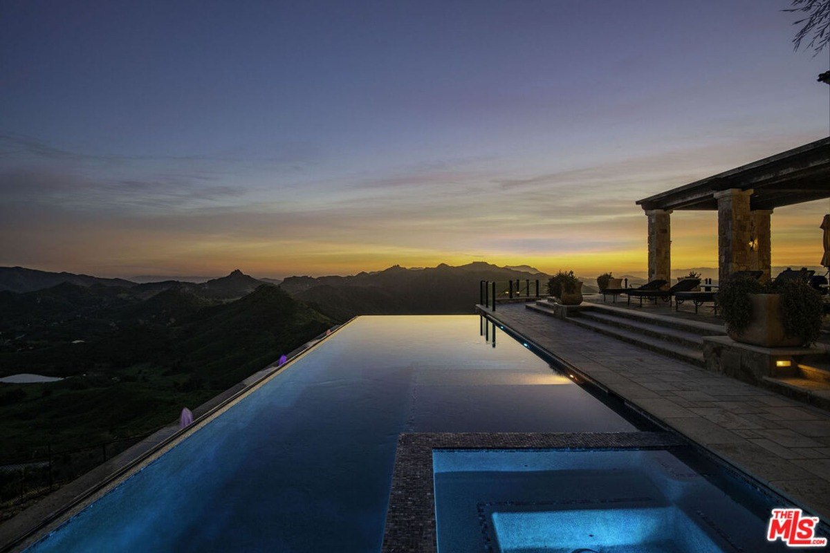 Infinity pool and spa overlook a mountain range at sunset.