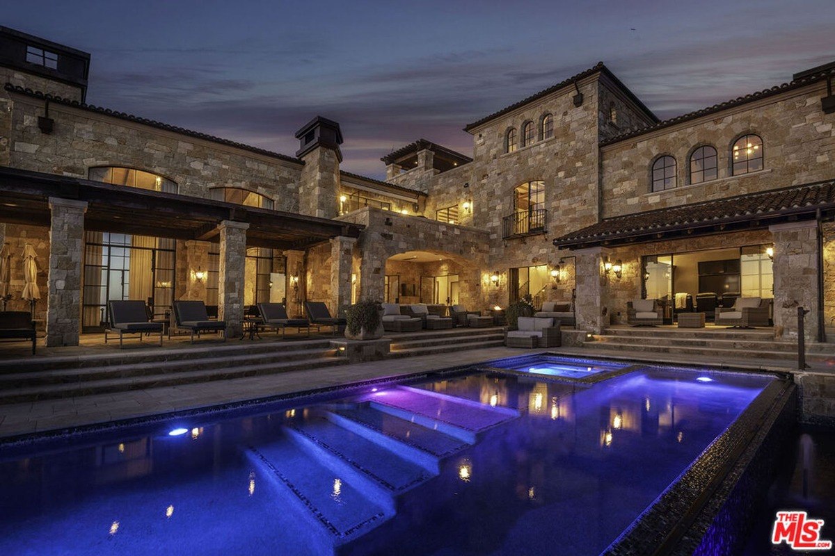 Luxurious mansion with a large pool and outdoor seating area at night.