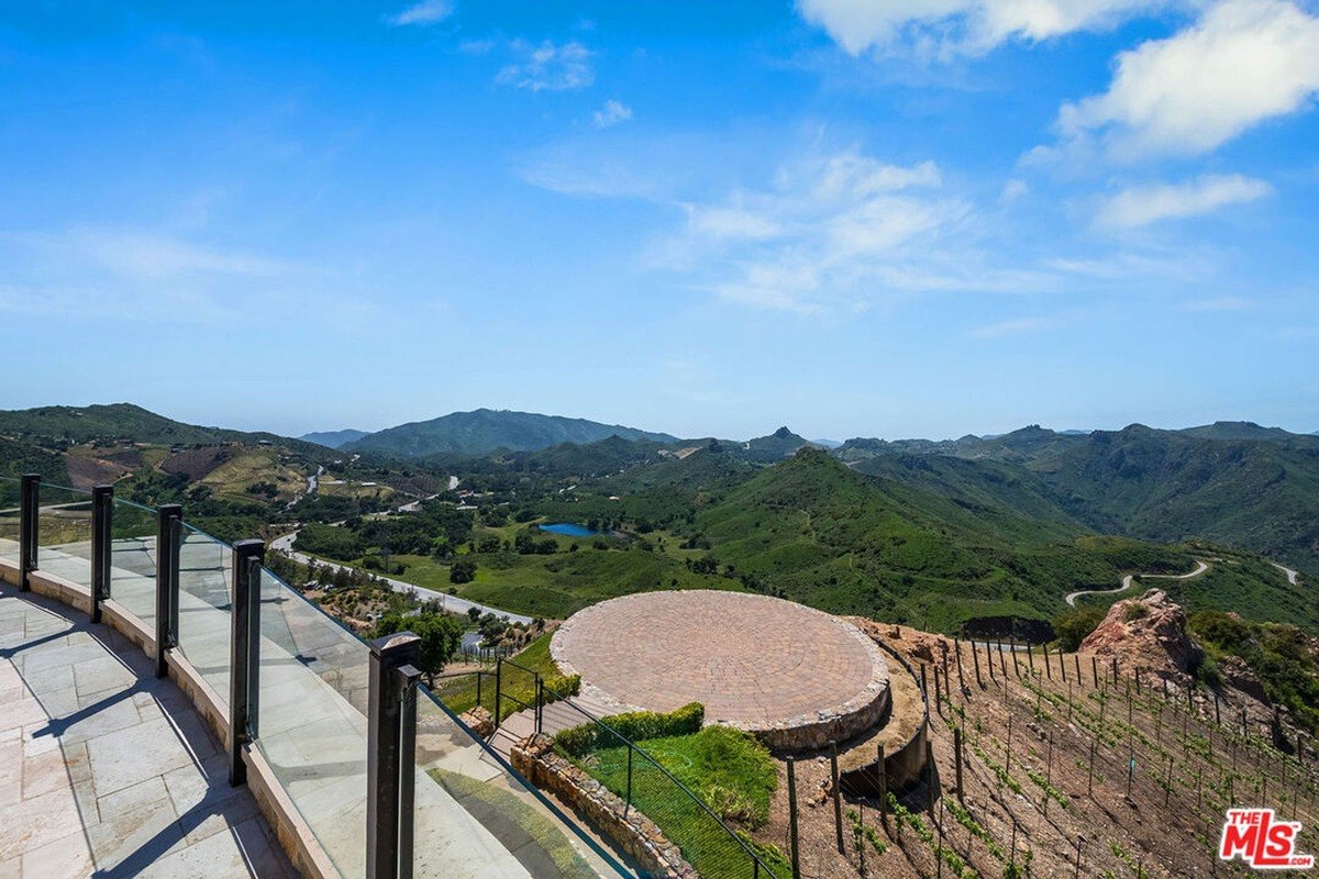 Circular viewing platform overlooking a scenic valley with rolling hills, vineyards, and a lake.