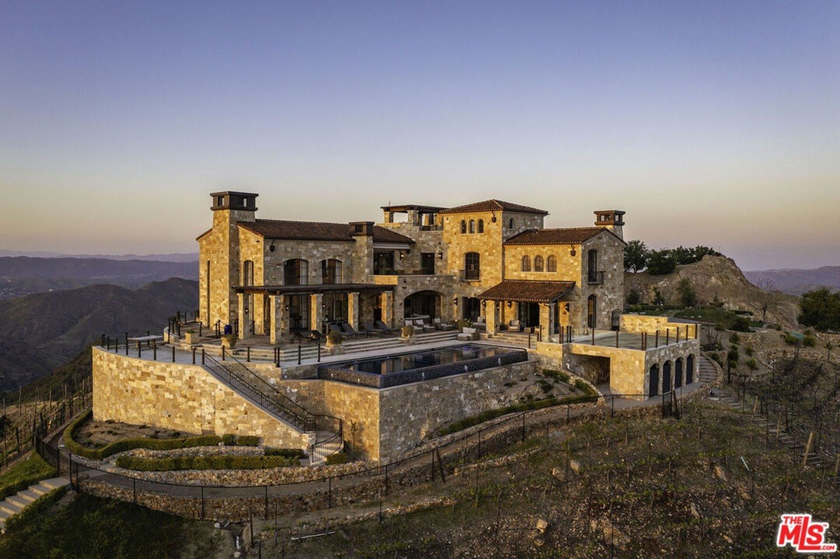 Mansion with a stunning infinity pool at dusk, offering breathtaking views of a mountain range.