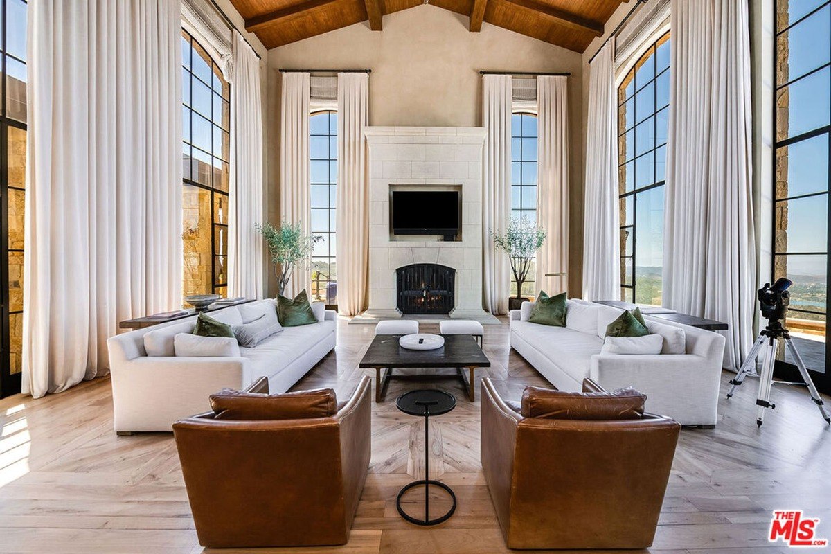 Spacious living room with high ceilings, large draped windows, and a central fireplace flanked by seating.