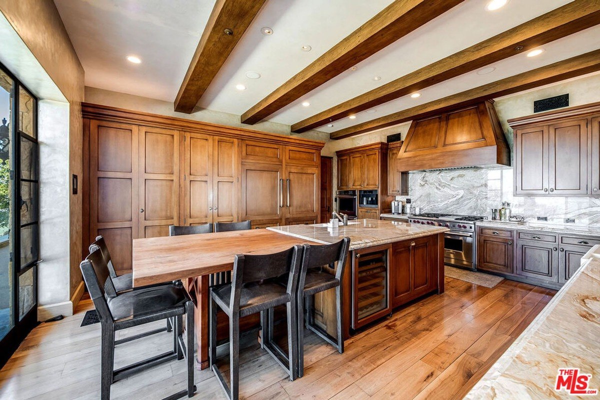 Kitchen featuring rich wood cabinetry, a large island with marble counters, and ceiling beams.