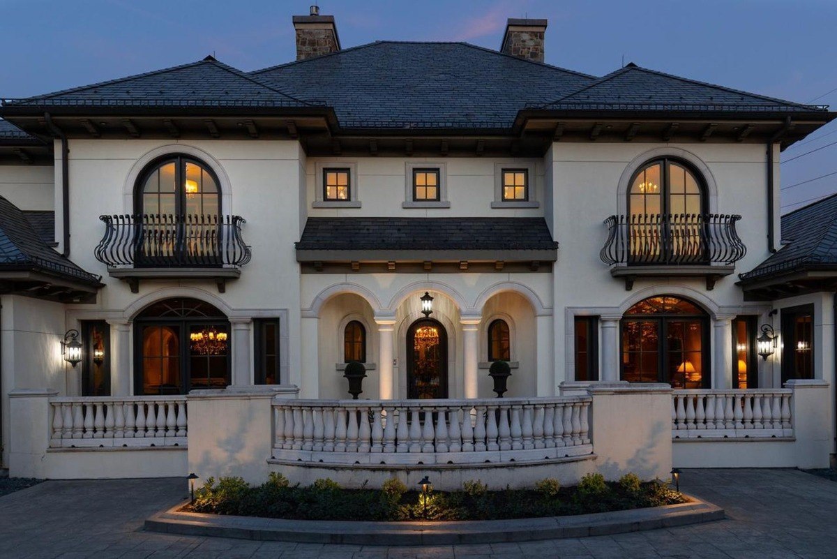 Grand white mansion with arched windows, wrought iron balconies, and a curved driveway exudes elegance and sophistication.