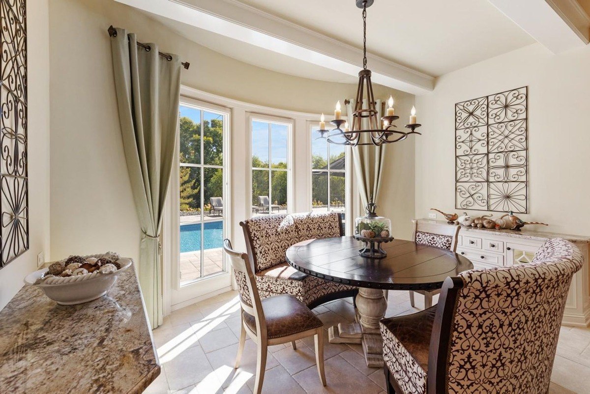 Sun-drenched breakfast nook with a round table, upholstered chairs, and large windows overlooking a pool creates a bright and inviting space.