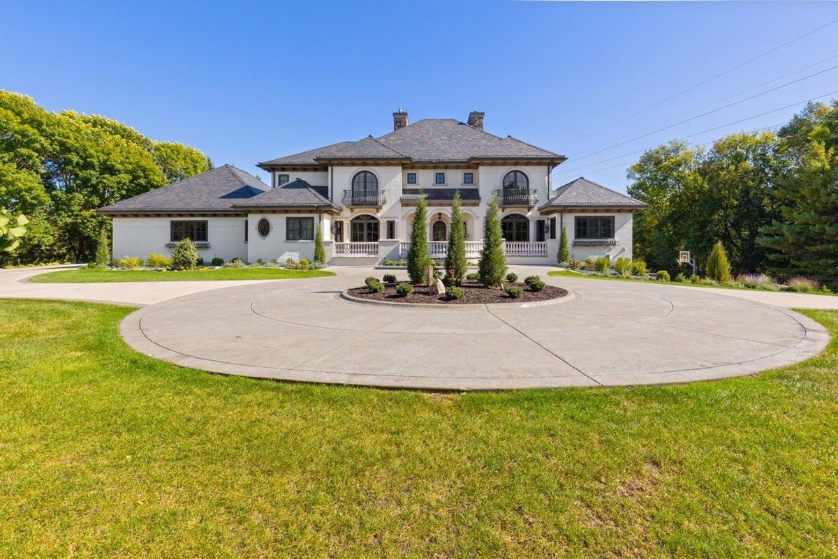 Stately home with a classic facade, a circular driveway, and manicured landscaping commands attention on a sunny day.