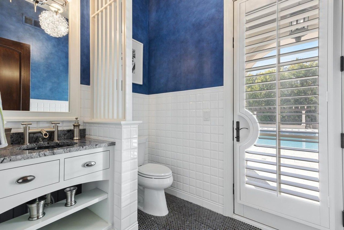 Stylish powder room with a bold blue wall, a white vanity, and a door leading to a poolside view offers a touch of luxury.