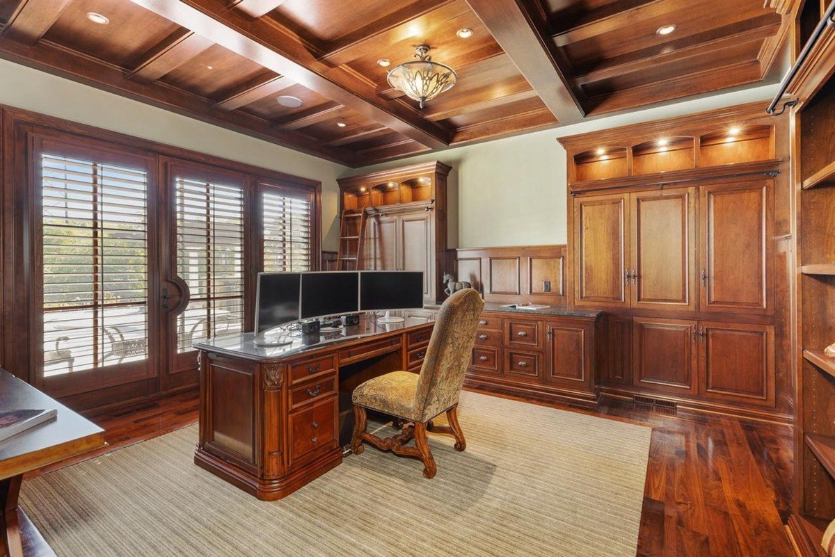 Home office with a coffered ceiling, built-in bookshelves, and a large desk provides a sophisticated workspace.