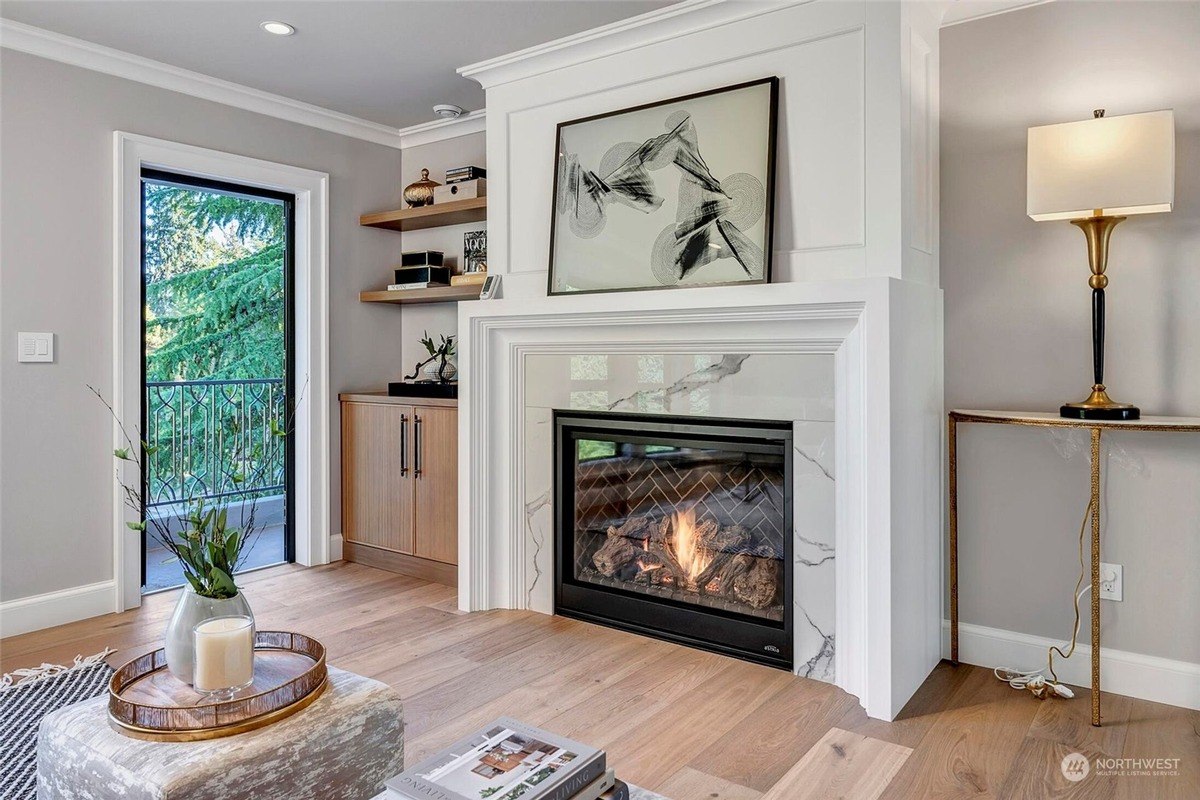 Living room has fireplace with marble surround, wood floors, and large window. 