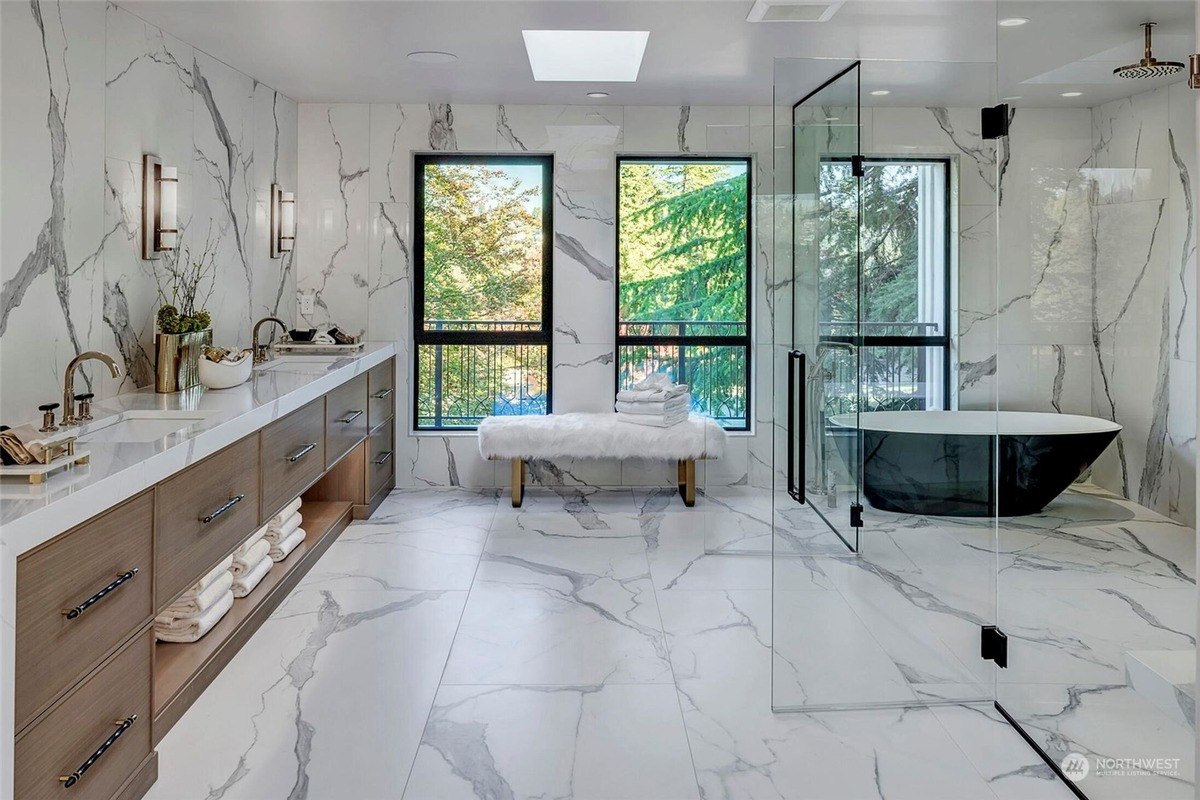 Bathroom has marble floors and walls, double vanity, free-standing tub, and glass shower.