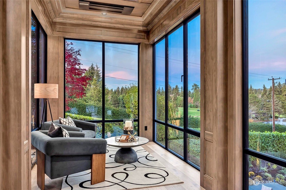 Sunroom has wood walls, large windows with views of trees and a golf course, and a gray sofa.coldwellbanker-medina-wa-jan0825-22