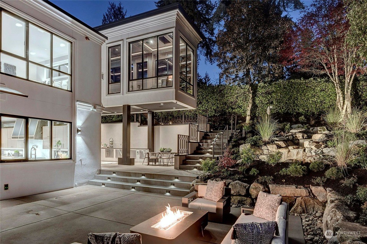 Home has a modern design, outdoor patio with fire pit, and a landscaped backyard at night.