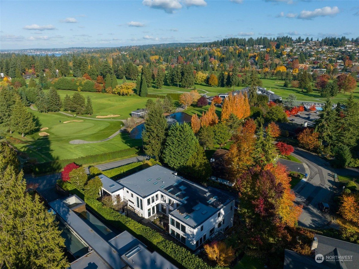 Mansion with a flat roof, surrounded by a vibrant fall landscape, overlooking a golf course and a lake.