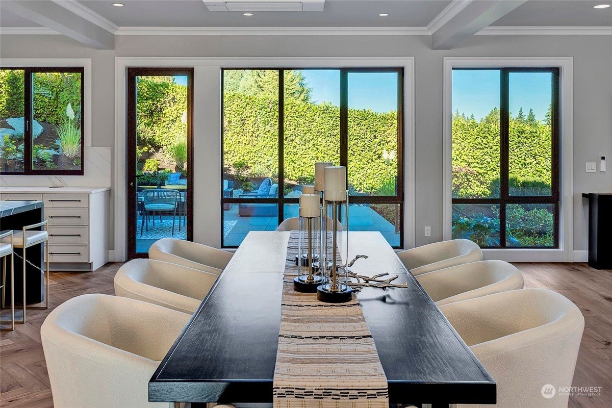 Dining area has long dark wood table with off-white chairs, and large windows overlooking a patio. 