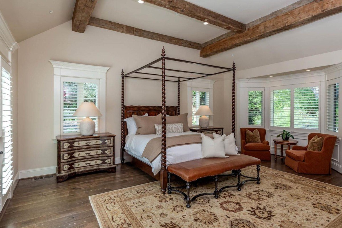 Spacious primary bedroom with a canopy bed, exposed wood beams, and seating area.