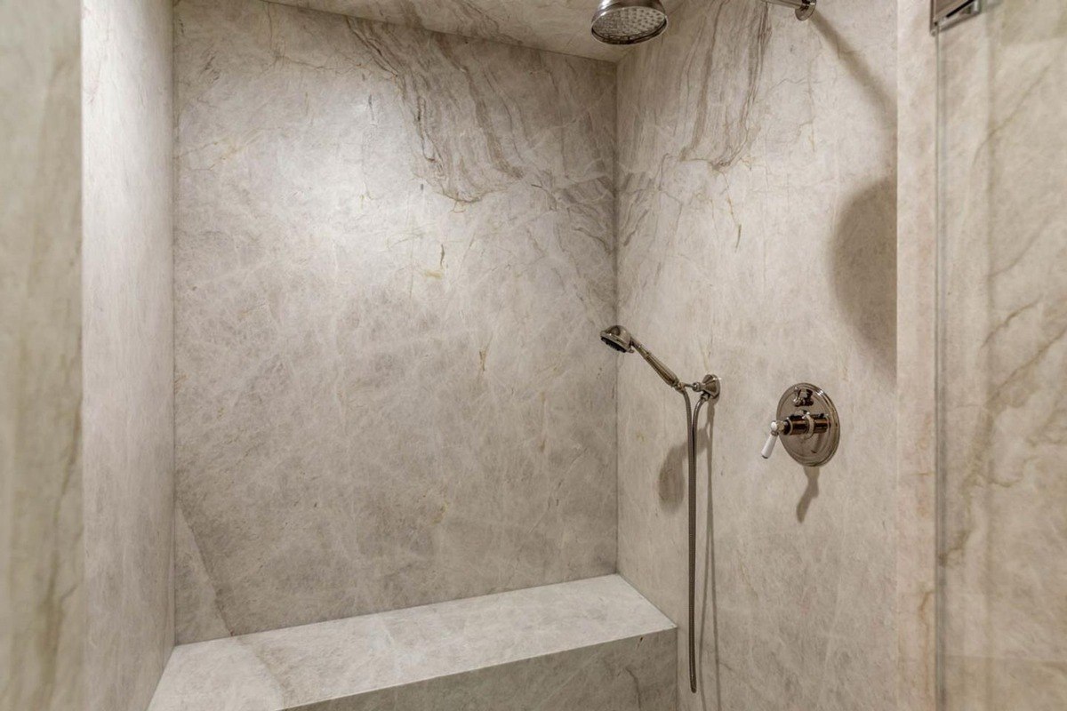 Marble walk-in shower with a built-in bench and rainfall showerhead.