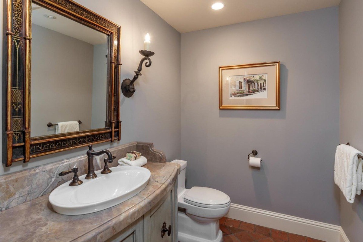 Powder room with a decorative mirror, sconce lighting, and marble-topped vanity.