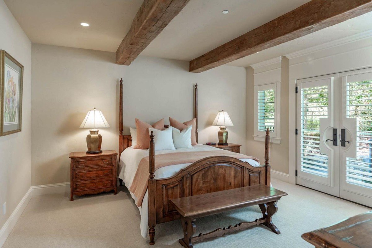 Cozy guest bedroom with a four-poster bed, exposed beams, and French doors.