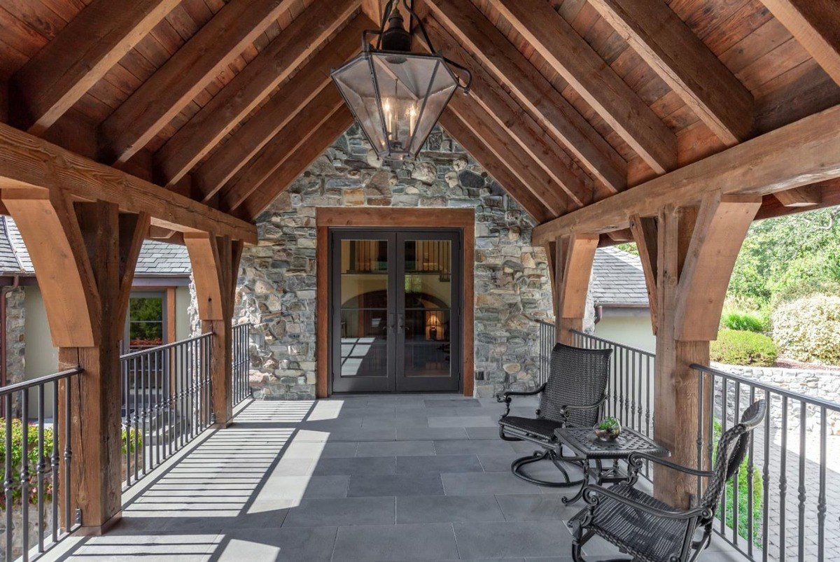 Covered balcony with wood beams, stone walls, and outdoor seating.