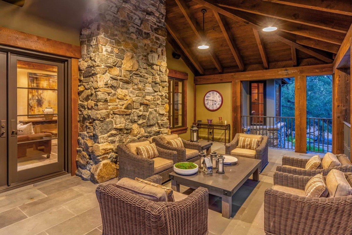 Outdoor seating area under a wood-beamed ceiling with stone accents and a fire feature.