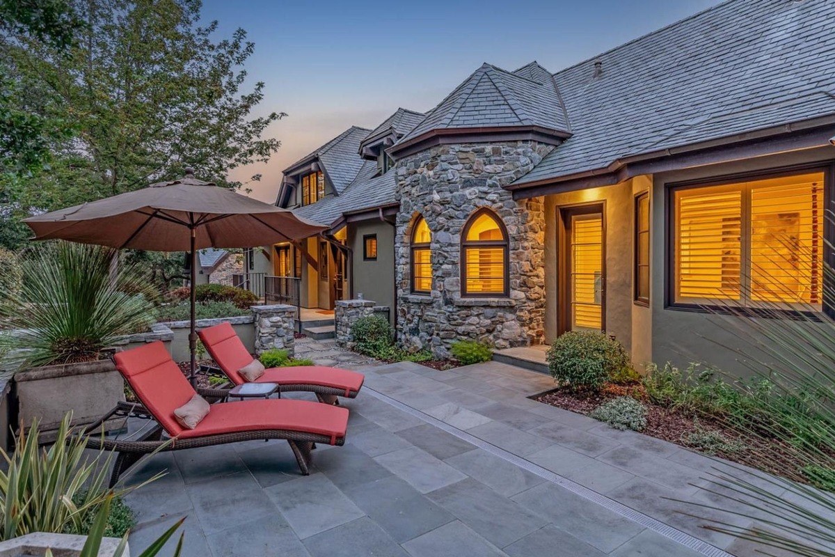 Side patio with loungers a side area with red lounge chairs and umbrella complements the stone exterior.