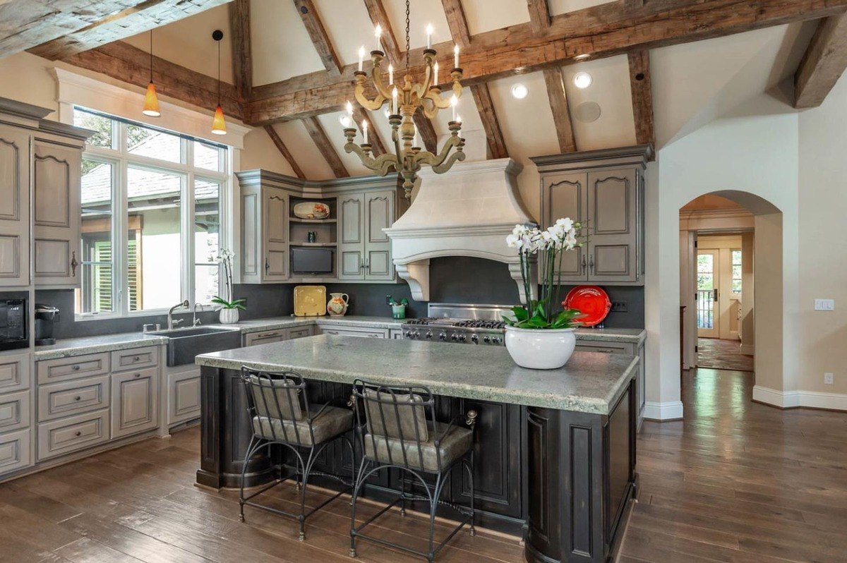 Kitchen with exposed beams, a large island, and rustic cabinetry.