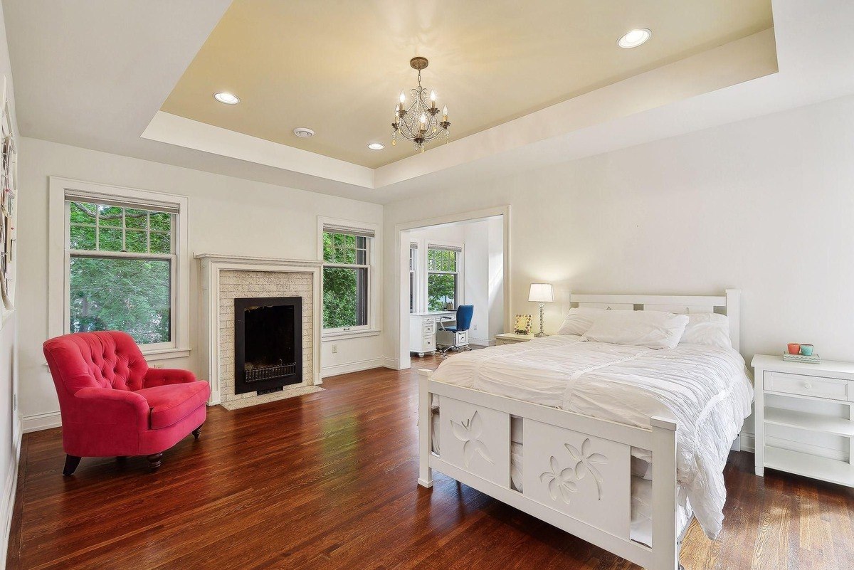 Bedroom with hardwood floors, a white bed, and a pink armchair.