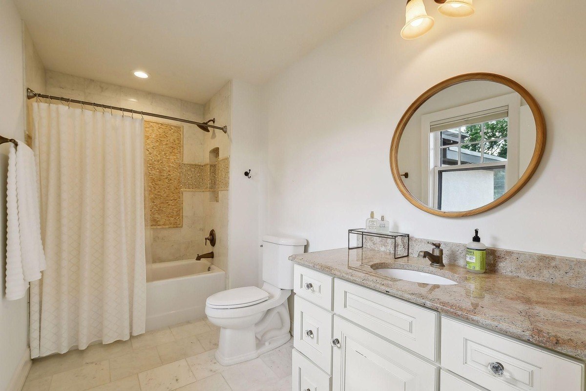 Bathroom features granite countertops, white cabinets, and a shower with a patterned tile accent.