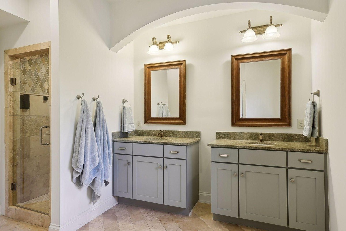 Bathroom boasts double vanities with granite countertops, gray cabinets, and framed mirrors.