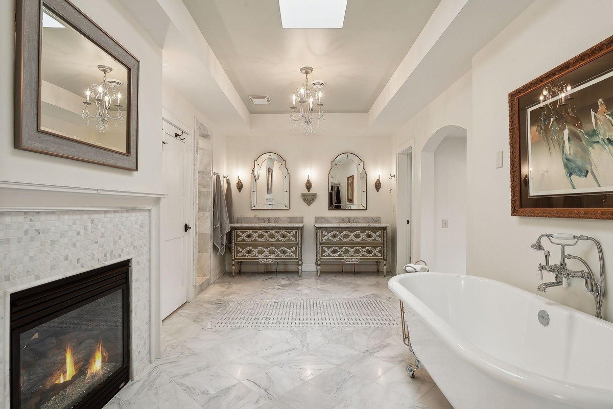 Bathroom with marble floors, double vanities, a freestanding tub, and a fireplace.