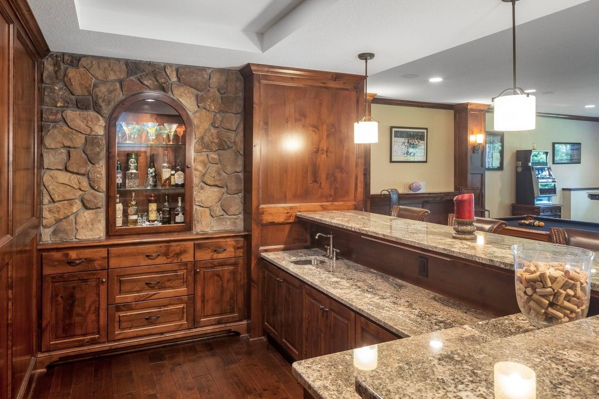 Home bar with wood cabinetry, stone accents, and granite countertops.