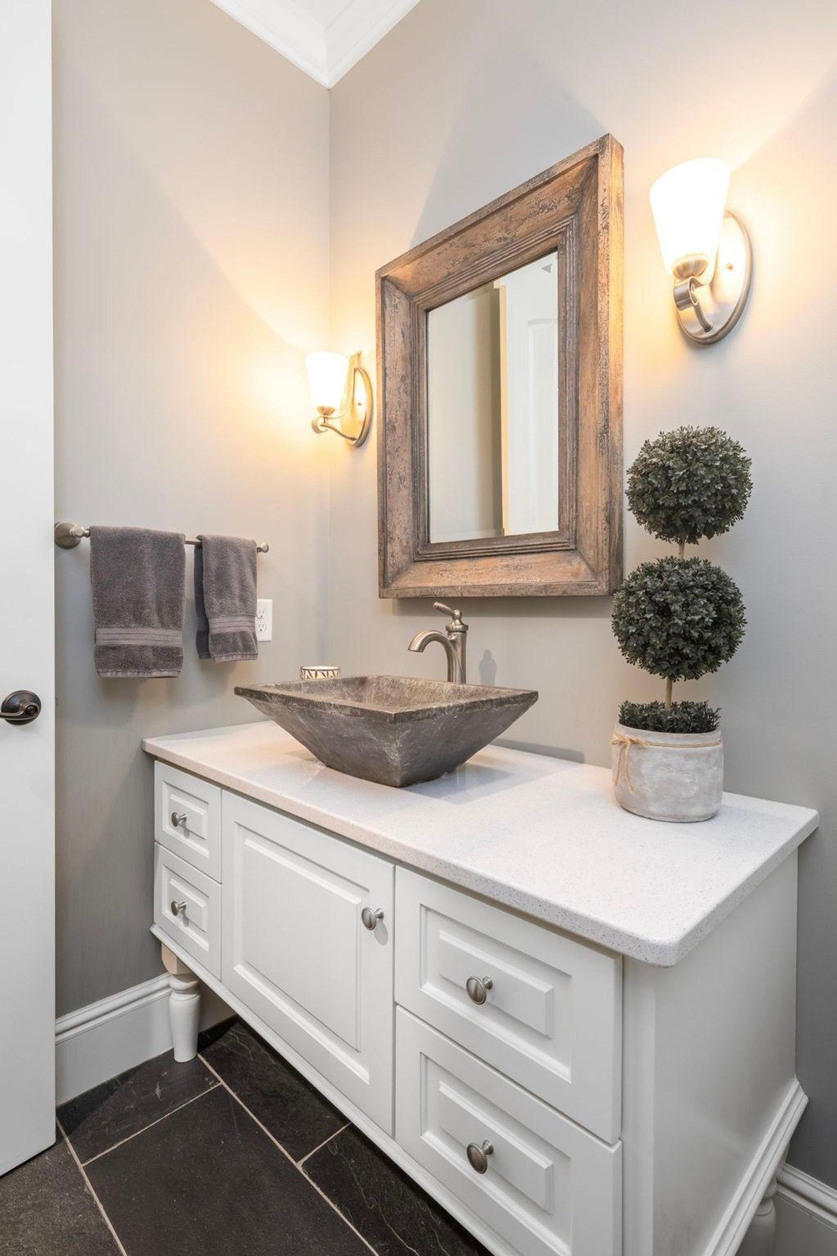 Stylish powder room with a rustic stone sink, a white vanity, and a large mirror creates a modern and elegant space.